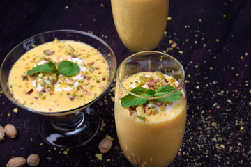 Mango yogurt dessert in a champagne glass topped with pistachios and mint against the dark background