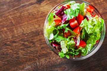 various fresh mix salad leaves with tomato in glass bowl on wooden background.