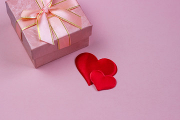 A gift in a beautiful box and red hearts on a pink background. Valentine's Day, International Women's Day.