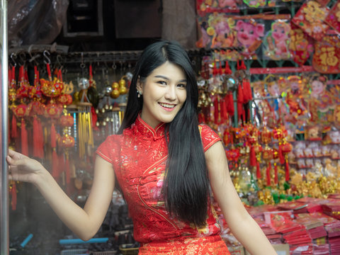 Portrait image pretty women are wearing red Cheongsam dress, happy smile while traveling in the night maket, in the Chinese New Year festival, with blurred soft of Sacred symbol hanging on the rail
