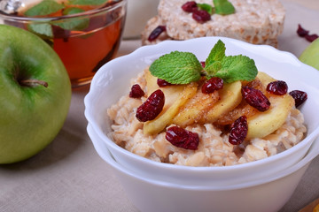 Porridge with caramelized apples and dried cranberries topped with mint surrounded by breakfast ingredients