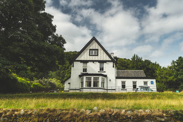 Obraz premium White traditional Irish house among trees and fields. Northern Ireland. Stunning ethnic building among the wild nature environment. Amazing countryside landscape. Modern Irish architecture.