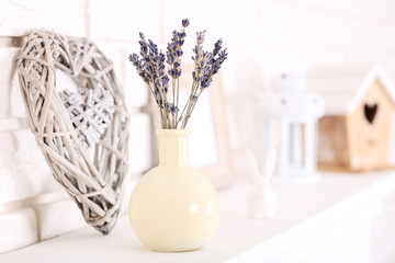 Lavender flowers in vase with decorative heart on white fireplace