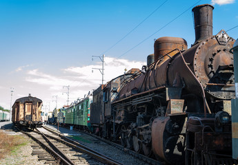 Fototapeta na wymiar Old rusty steam locomotive beside a railway station platform. Retro train.