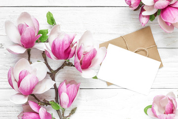 blank white greeting card with pink magnolia flowers and envelope on white wooden table. flat lay. top view © samael334