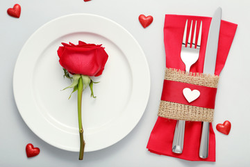 Red rose in white plate with kitchen cutlery on grey background