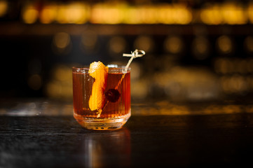 Glass of cocktail with whiskey decorated with orange peel and cherry