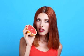 Beautiful redhaired woman with grapefruit on blue background