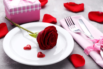 Red rose in white plate with ritchen cutlery on grey wooden table
