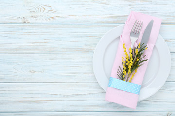 Kitchen cutlery with plate and mimosa flowers on wooden table