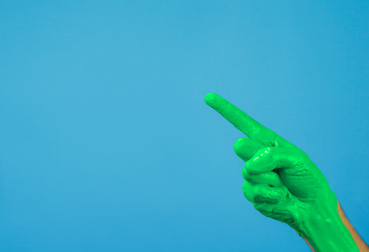 hand in green paint on a blue background, finger points to copy space