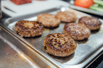 Beef round hamburger patties are cooked on a metal baking sheet