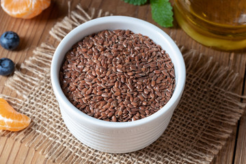 Flax seeds in a bowl, with flax seed oil in the background