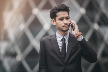 Young executive businessman using a mobile phone in the business district with skyscrapers buildings background