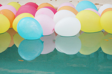 Lots of colorful balloons floating on the water with reflections.