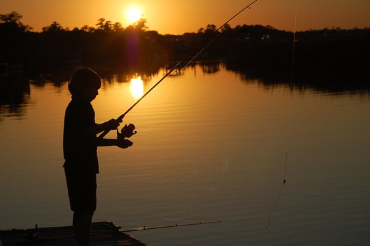 Silhouette of boy fishing off a dock at sunset.