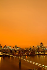 London Millenium Bridge against city in orange sunset as viewed from tate modern balcony