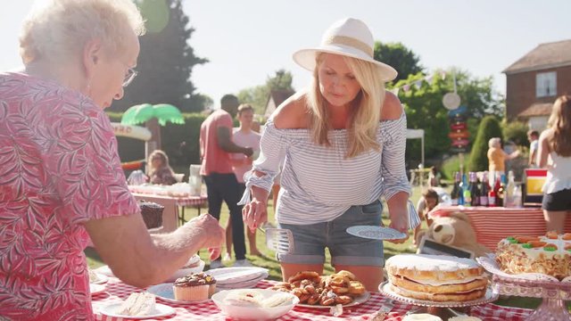 Slow Motion Shot Of Mature Woman Serving On Cake Stall At Busy Summer Garden Fete