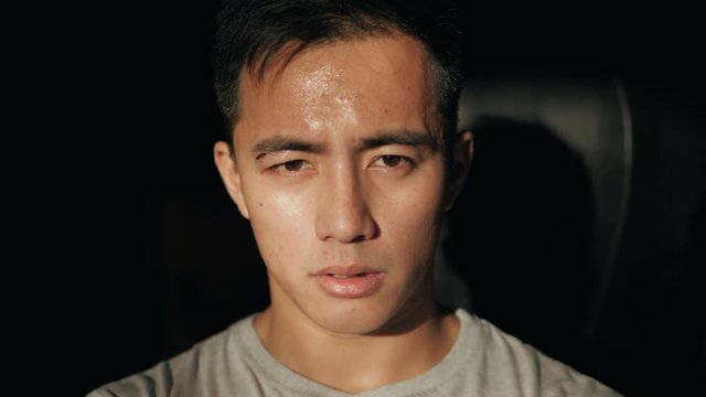 Portrait of asian handsome man standing at the sun light wear boxing glove in the gym. Tired chinesse korean man close up
