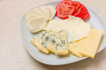 Assorted cheese sliced cheese with tomato on white plate