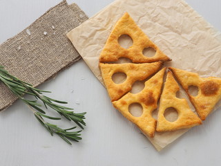 Cheese slice shape crackers upon parchment with rosemary stem
