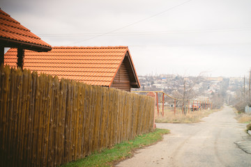 Rural street. Fence made of sharp wooden stakes. House with a red tiled roof
