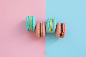 Obraz premium Sweet colorful French macaroon biscuits on pink and blue pastel background, top view. Flay lay selection of macarons.