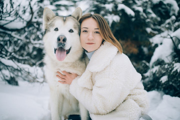 Girl is hugging dog Alaskan Malamute in winter forest.