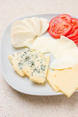 Assorted cheese sliced cheese with tomato on white plate