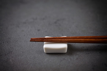 Wooden chopsticks and chopstick rest on black stone background. Close up. Copy space. 