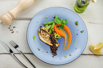 Gourmet grilled seabass fish fillet steak and vegetable salad. Delicious healthy meal made of seafood and vegetables on a rustic table.Directly above top view shot.