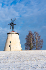 Fototapeta na wymiar Empty Countryside Landscape in Sunny Winter Day with Snow Covering the Ground with Big Abandoned Windmill in Background