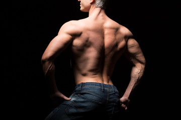 Fototapeta na wymiar Handsome power athletic man in dramatic light. Strong bodybuilder with perfect shoulders, biceps, triceps, back, delta and chest. Strength and motivation. Bottom view