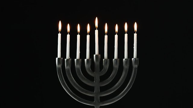 A row of nine white candles burning in a menorah are blown out, front view