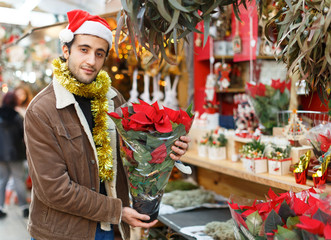 Young man in Christmas hat buying  flowers and decoration at Christmas fair