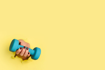 Woman hand holding blue dumbbell on yellow background. Fitness, sport, healthy lifestyle, diet concept. Banner with copy space