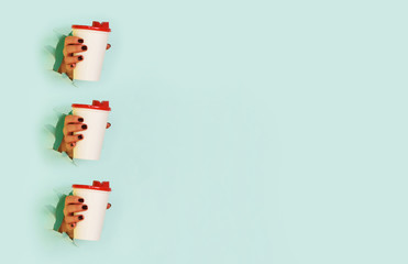 Pattern of female hand holding white paper mug on blue background. Take away coffee cup concept. Mock up with copy space