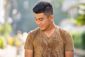 Happy young Asian man thinking and looking down outdoors