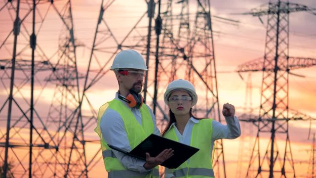 Power lines and two specialists engineers working on renewable energy development during sunset