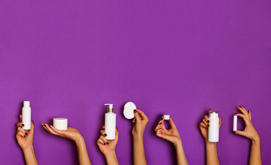 Female hands holding white cosmetics bottles - lotion, cream, serum on violet background. Square...