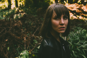Handsome young girl walking in the forest looks at the camera. Colorful sunny green background. 