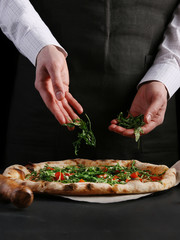 chef sprinkles arugula on traditional pizza. making pizza concept