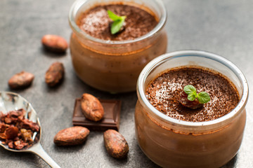 Chocolate dessert panna cotta in glass jars with raw cocoa beans