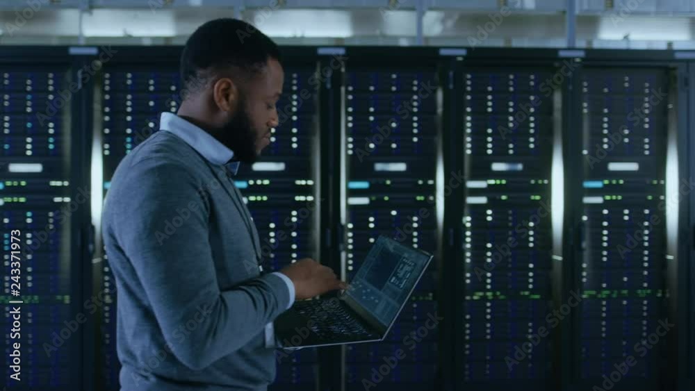 Poster Black Data Center IT Technician Walking Through Server Rack Corridor with a Laptop Computer