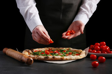 Obraz na płótnie Canvas chef put ingredients on pizza. chef in apron and white shirt decorating pizza with tomatoes cherry and arugula