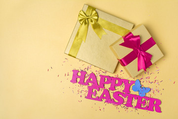 Fototapeta na wymiar Pink text of happy easter and golden gift boxes with satin bows and sugar sprinkles