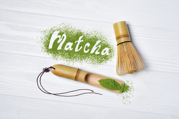 Lettering from green matcha tea with bamboo whisk and scoop on white wood