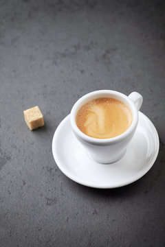 Cup of coffee and a brown sugar cube on black stone background. Close up. Copy space
