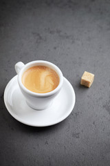 Cup of coffee and a brown sugar cube on black stone background. Close up. Copy space
