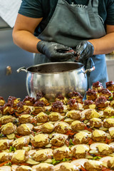 Female Chef Putting Ingredients of Burgers on a Sliced Bread Spread on a Table in Black Gloves - Concept of the Hard Working Person and the Hygiene in the Kitchen